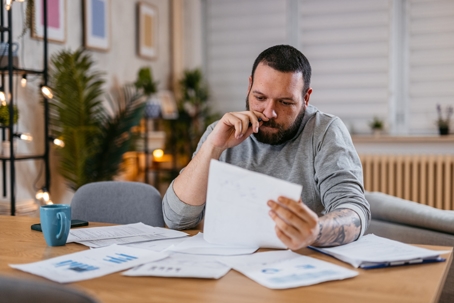 Man checking personal finances at home, while sitting at the table, holding the paper.